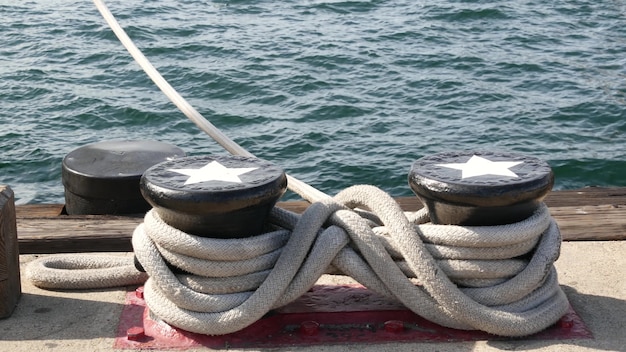 Nudo de cuerda atado en bolardo metálico, puerto de San Diego. Barco náutico amarrado, flota naval, bandera de Estados Unidos.