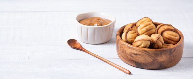 Nueces al horno con leche hervida en un recipiente de madera y caramelo sobre una mesa blanca. Vista frontal y espacio de copia. imagen horizontal