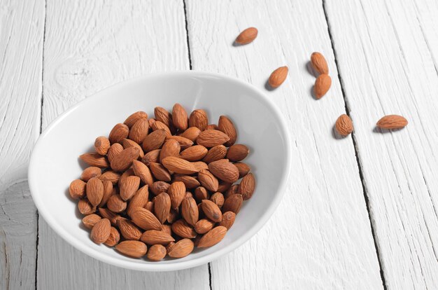 Nueces de almendra en un recipiente sobre la mesa de madera blanca. Comida sana