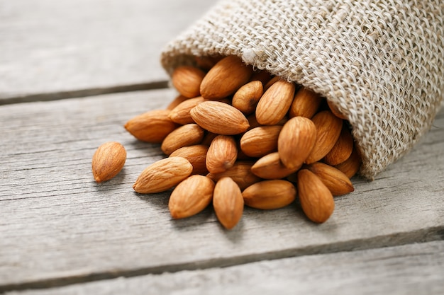 Nueces almendras en una bolsa de arpillera en un gris de madera.