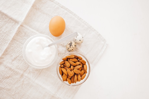 Nueces, almendras, crema agria o yogur, pollo y huevos de codorniz en una toalla de cocina de lino sobre una mesa blanca. Alimentos y nutrientes saludables para una nutrición adecuada del concepto de cerebro y cuerpo