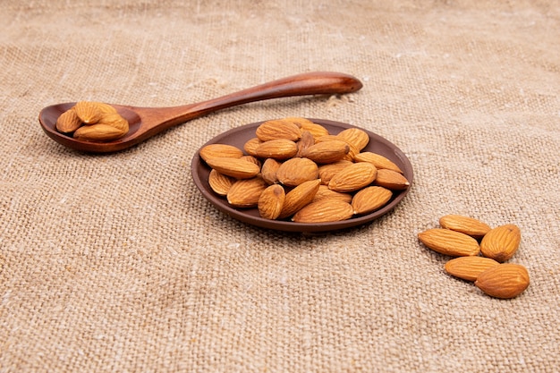 Nueces almendras en una cuchara de madera y una placa de barro marrón sobre arpillera vieja.