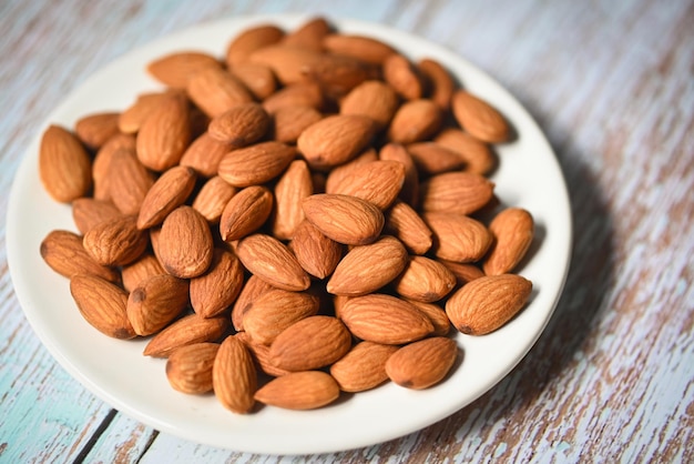 Nueces de almendras en palte blanco Deliciosas almendras dulces en el fondo de la mesa de madera nuez de almendra tostada para comida saludable y merienda