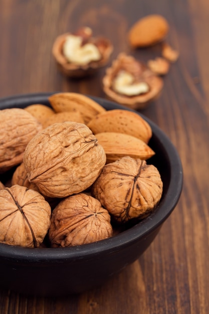 Nueces y almendras en un tazón negro sobre una superficie de madera marrón