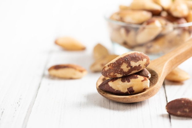 Nueces de Brasil en cuchara de madera y espacio para texto sobre fondo blanco de madera