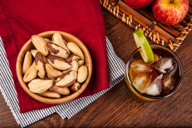 Nueces brasileñas en una mesa de madera con manzanas y té helado en el fondo.