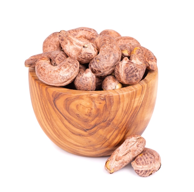 Nueces de cajú con cáscara en tazón de madera aislado sobre fondo blanco Nueces de cajú tostadas y saladas