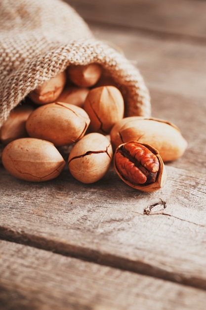 Las nueces se derraman de una bolsa de arpillera sobre una mesa de madera en primer plano.