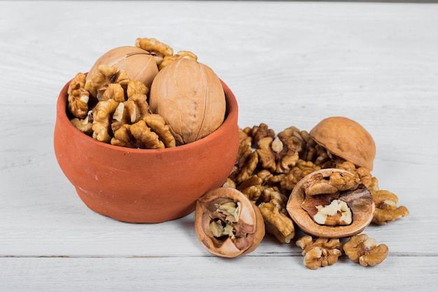 Nueces enteras y granos sobre una nuez de fondo de madera blanca sobre una mesa vieja y clara en una olla de barro