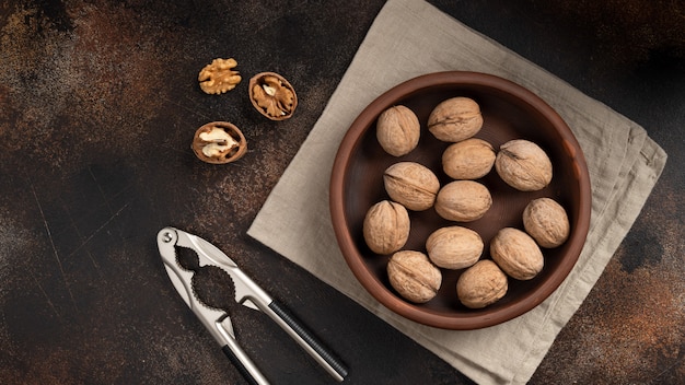 Nueces enteras y nueces rotas con un cascanueces en una pared marrón