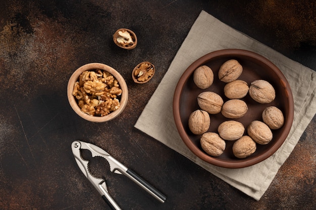 Nueces enteras, nueces rotas y granos pelados con un cascanueces en una pared de hormigón marrón. comida sana