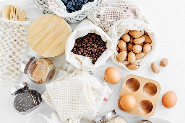 Nueces, frutos secos y cereales en bolsas de algodón ecológico y frascos de vidrio sobre mesa blanca en la cocina. Compras de alimentos sin desperdicio. Vida sin desperdicios