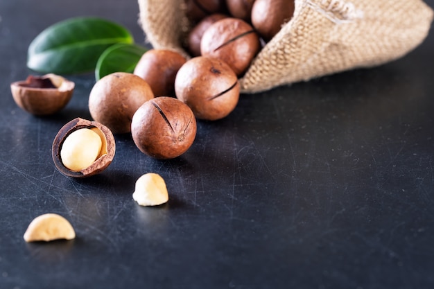 Nueces de macadamia australianas con hojas verdes derramadas de la bolsa