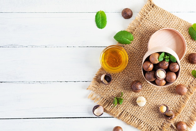 Nueces de macadamia con cáscara con hojas de menta y miel en madera