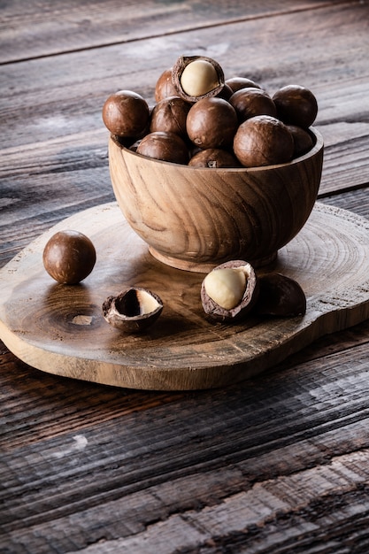 Nueces de macadamia enteras en un tazón en la vieja mesa rústica de madera