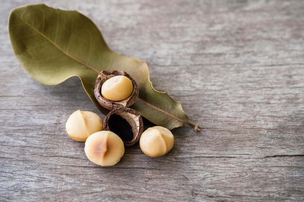 Nueces de macadamia orgánicas peladas con hojas sobre mesa de madera