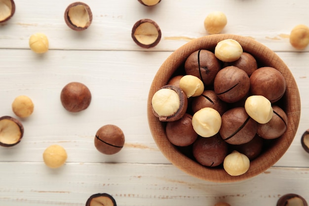 Nueces de macadamia peladas en cuenco de madera sobre fondo blanco.