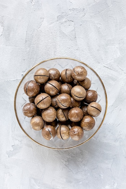 Nueces de macadamia saladas tostadas con cáscara en un tazón de vidrio sobre fondo gris, concepto de alimentación saludable comida vegana. Vista superior