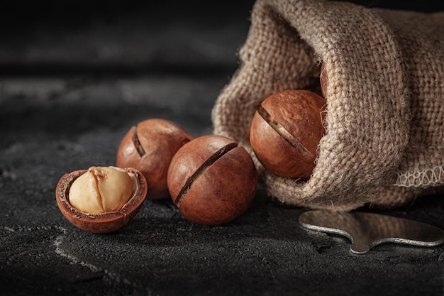 Nueces de macadamia vertidas de fondo de pizarra de piedra de saco de arpillera