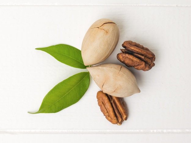 Nueces de pacana con dos hojas sobre una mesa de madera blanca. Comida vegetariana.