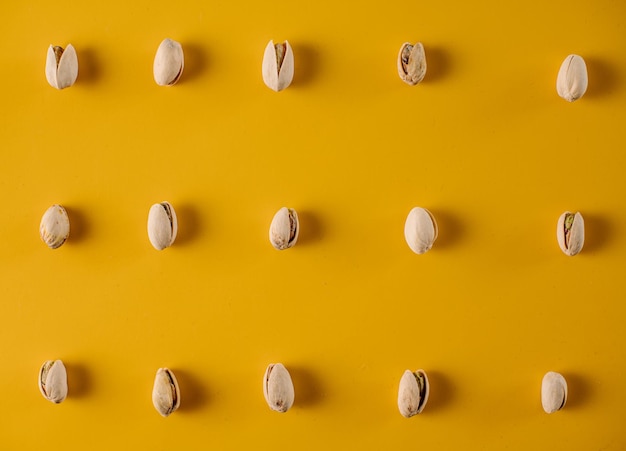 Nueces de pistacho dispuestas en filas sobre un fondo amarillo