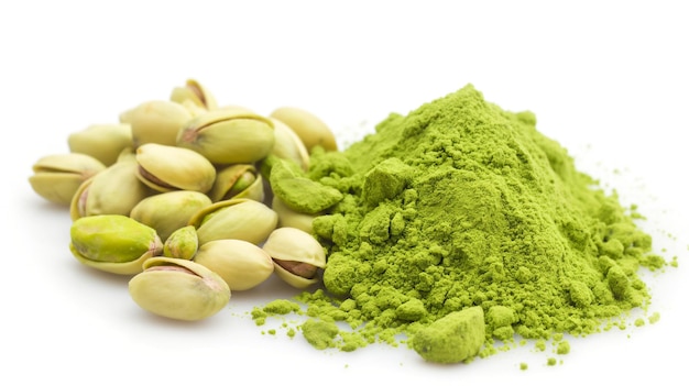 Foto nueces de pistacho junto a un montículo de polvo de pistacho verde vibrante sobre un fondo blanco