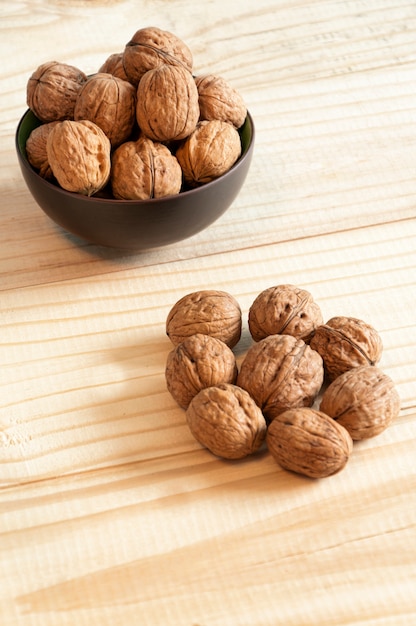 Nueces en un recipiente de color marrón oscuro y sobre una mesa de madera