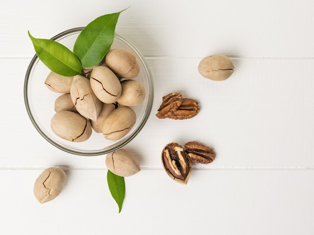 Nueces, un recipiente de vidrio y hojas verdes sobre una mesa de madera blanca. Comida vegetariana.