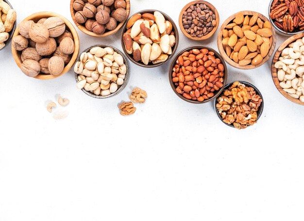 Nueces en tazones Almendras avellanas nueces y otra mezcla de refrigerios de alimentos saludables en el espacio de copia de la vista superior de la mesa blanca