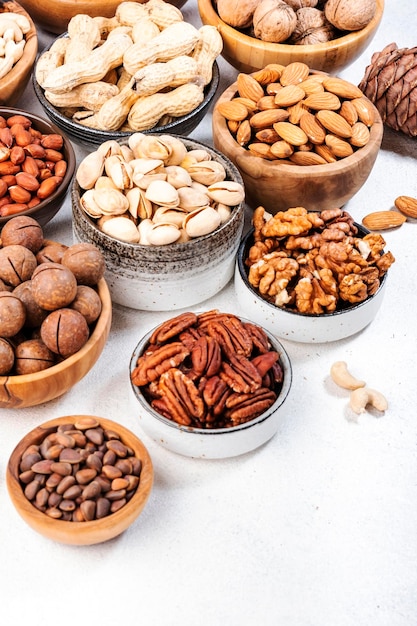 Nueces en tazones Almendras avellanas nueces y otra mezcla de refrigerios de alimentos saludables en el espacio de copia de la vista superior de la mesa blanca