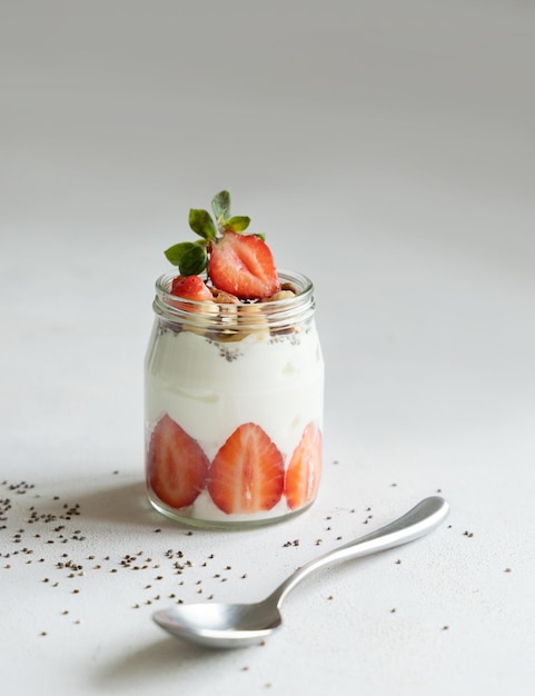 Nueces de yogur griego y fresas en un frasco de vidrio sobre una mesa blanca cerca del espacio de copia