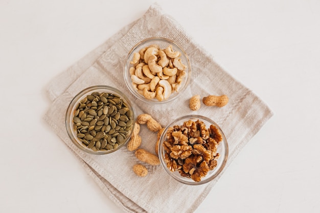 Nüsse und Essig auf einem Leinengeschirrtuch auf einem weißen Tisch. Walnüsse, Cashewkerne und Kürbiskerne für die richtige Ernährung. gesunde Lebensmittel und Nährstoffe für Gehirn und Körper