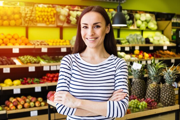 En nuestra tienda, los productos más frescos Hermosa vendedora joven y sonriente en el fondo del supermercado mira la cámara