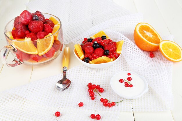 Nützlicher Obstsalat in Glasbecher und Schüssel auf Holztisch in der Nähe