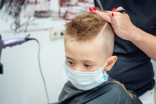 Nueva adaptación normal a la vida normal después del bloqueo pandémico. Niño cortarse el pelo con máscara.