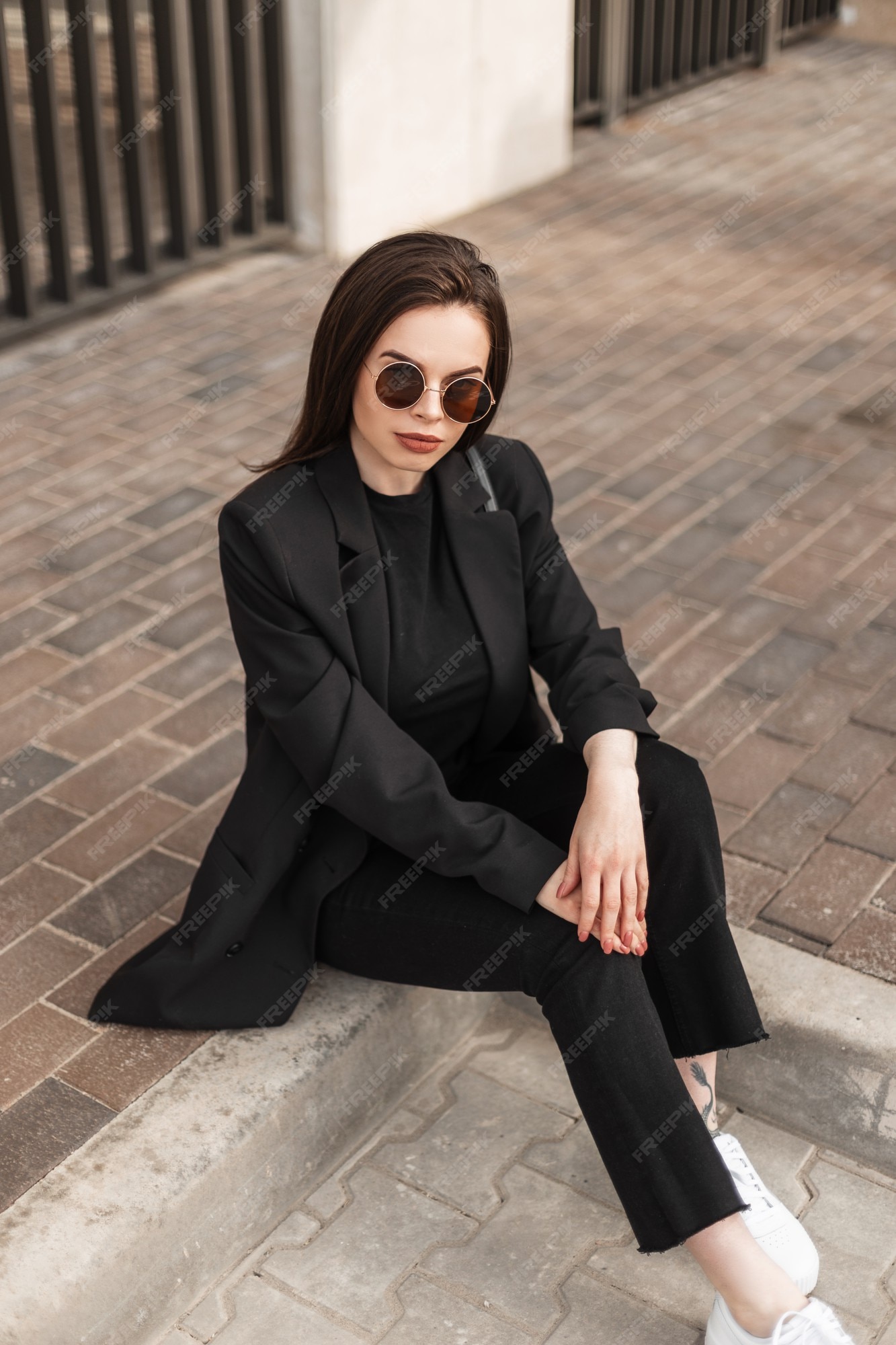 Nueva colección juvenil de elegantes chaquetas de mujer. elegante mujer hermosa en pantalones y camiseta con blazer negro moda se sienta en la calle. | Foto Premium