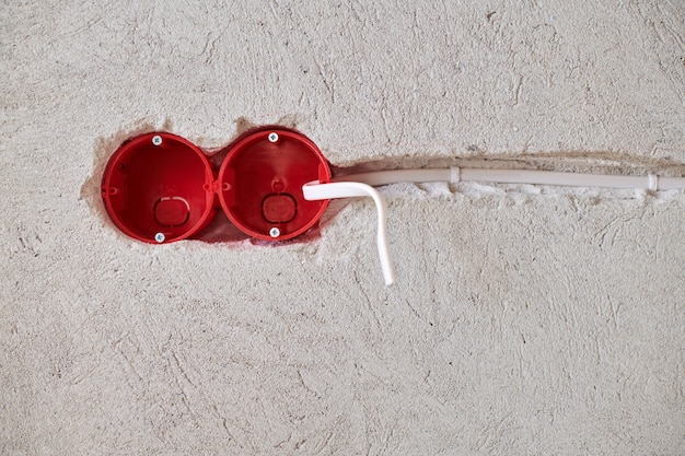 Nueva instalación de cableado eléctrico, caja de enchufes de plástico y cables eléctricos para futuros enchufes en pared enlucida, concepto de renovación del hogar.