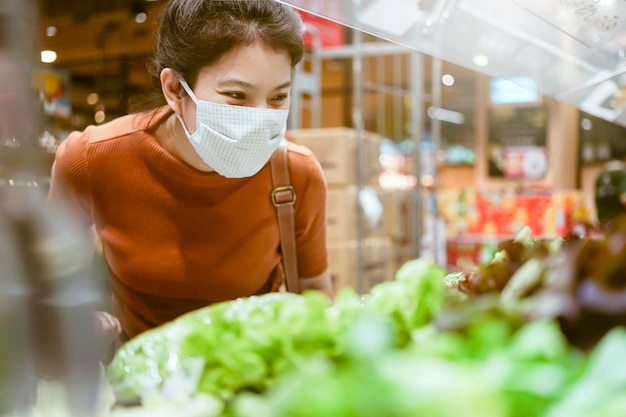 Nueva normalidad después de la epidemia de covid, joven mujer asiática inteligente que compra un nuevo estilo de vida en el supermercado con protector facial o protección con máscara, elija vegetales frescos de frutas, nuevo estilo de vida normal