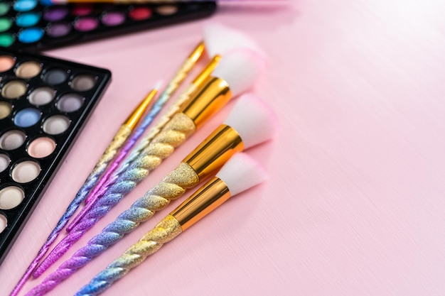 Foto nueva paleta de sombras de ojos con pinceles de maquillaje sobre un fondo rosa.