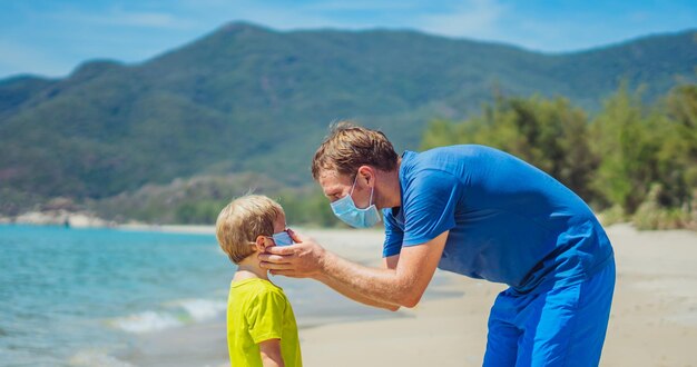Nueva seguridad de la era de la realidad normal durante la pandemia mundial COVID 19 El padre acompaña a su hijo poniéndose una máscara para proteger y prevenir el coronavirus incluso caminando en la playa de arena natural cerca del parque forestal en un día soleado