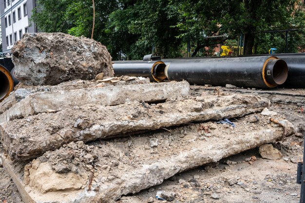 Nuevas tuberías de agua negras aisladas y losas de hormigón en la carretera de la ciudad en verano. Concepto de infraestructura de alcantarillado urbano, modernización y reconstrucción del sistema subterráneo.