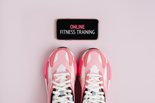 Nuevas zapatillas y smartphone sobre un fondo rosa. Aplicación para entrenar en interiores. Programa de fitness en línea