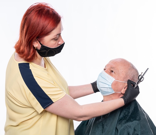 Nuevo concepto de corte de pelo normal. Peluquería mujer cortando el cabello a un hombre senior en mascarilla