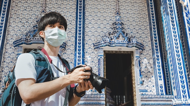 Foto nuevo concepto de viaje normal, hombre asiático viajero feliz con máscara y cámara de turismo en el templo wat pak nam khaem nu, chanthaburi, tailandia