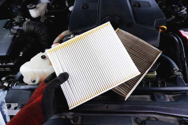 Nuevo filtro de aire en una mano y viejo filtro sucio colocado en el compartimiento del motor del automóvil