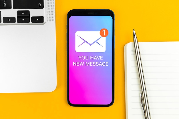 Nuevo icono de mensaje en la pantalla del teléfono móvil Concepto de Internet y tecnología de comunicación empresarial Mesa de oficina con foto de fondo de la vista superior del portátil