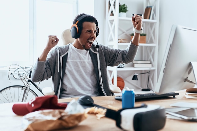 Nuevo logro. Feliz joven en ropa casual gesticulando y sonriendo mientras pasa tiempo en casa