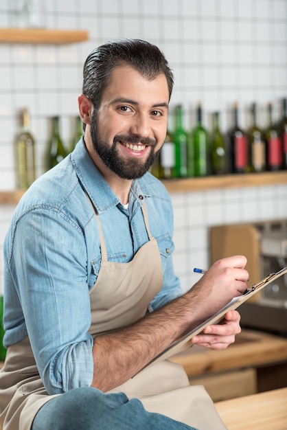 Foto nuevo menú. especialista creativo entusiasta alegre que tiene un día productivo mientras se sienta y escribe un nuevo menú para una cafetería agradable y cómoda