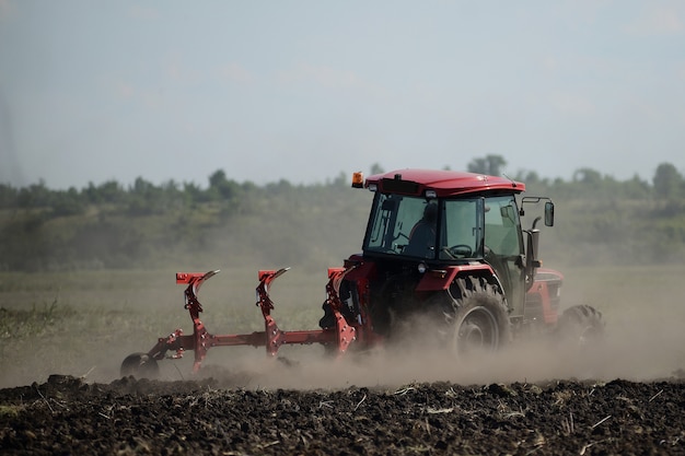 Nuevo tractor rojo en el campo trabajando. Tractor cultivando tierra y preparando un campo para plantar.