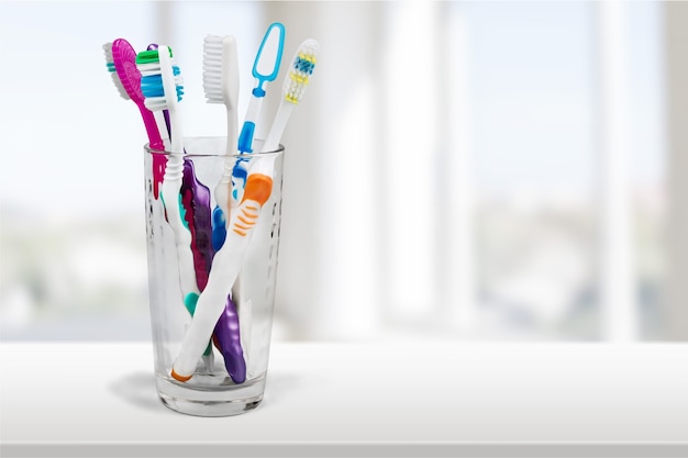 Nuevos cepillos de dientes de colores en un vaso en el fondo